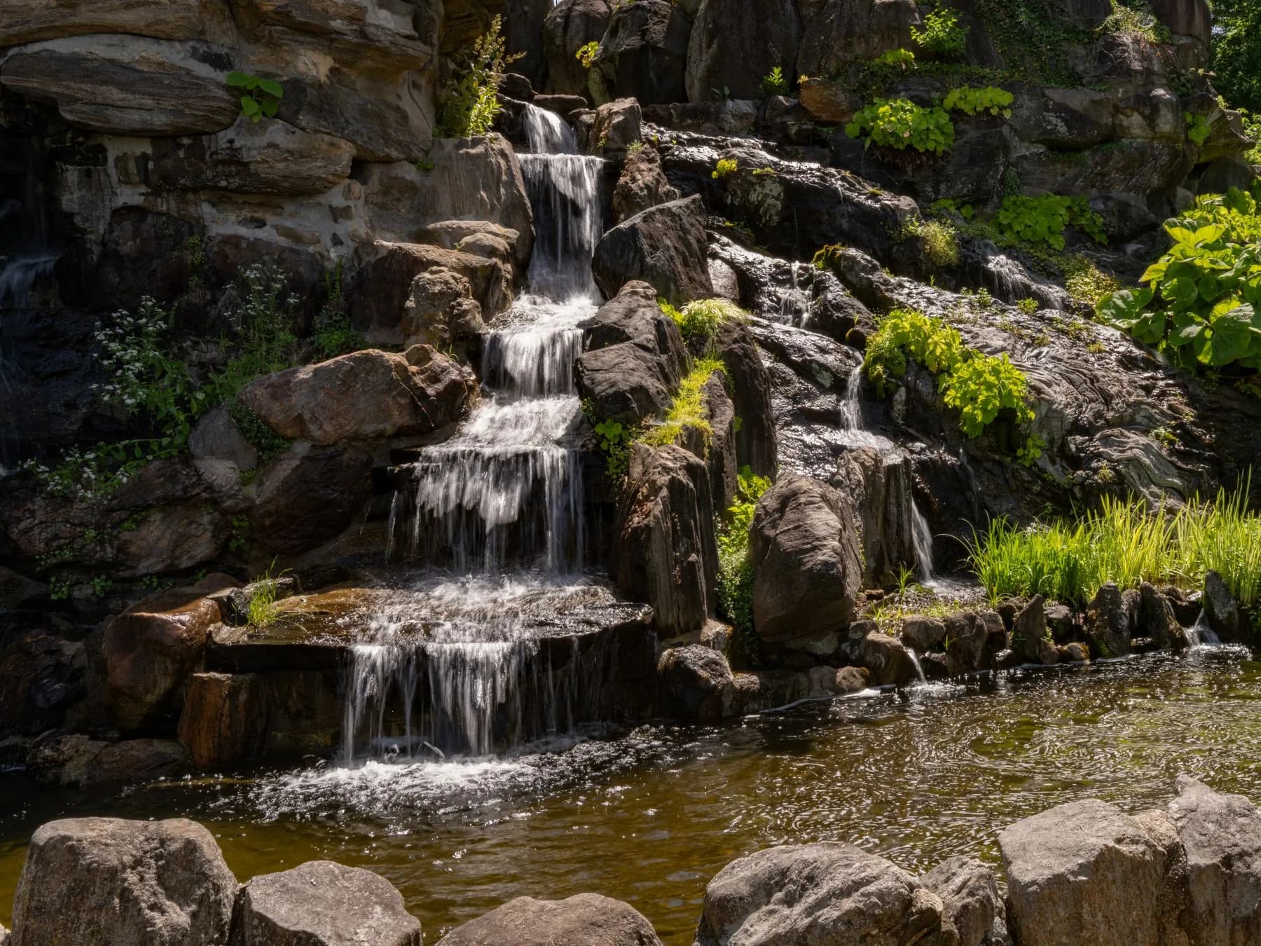Natural rock waterfall cascading through a planted private garden in Al Ain, built by Absher Landscaping from locally quarried stone