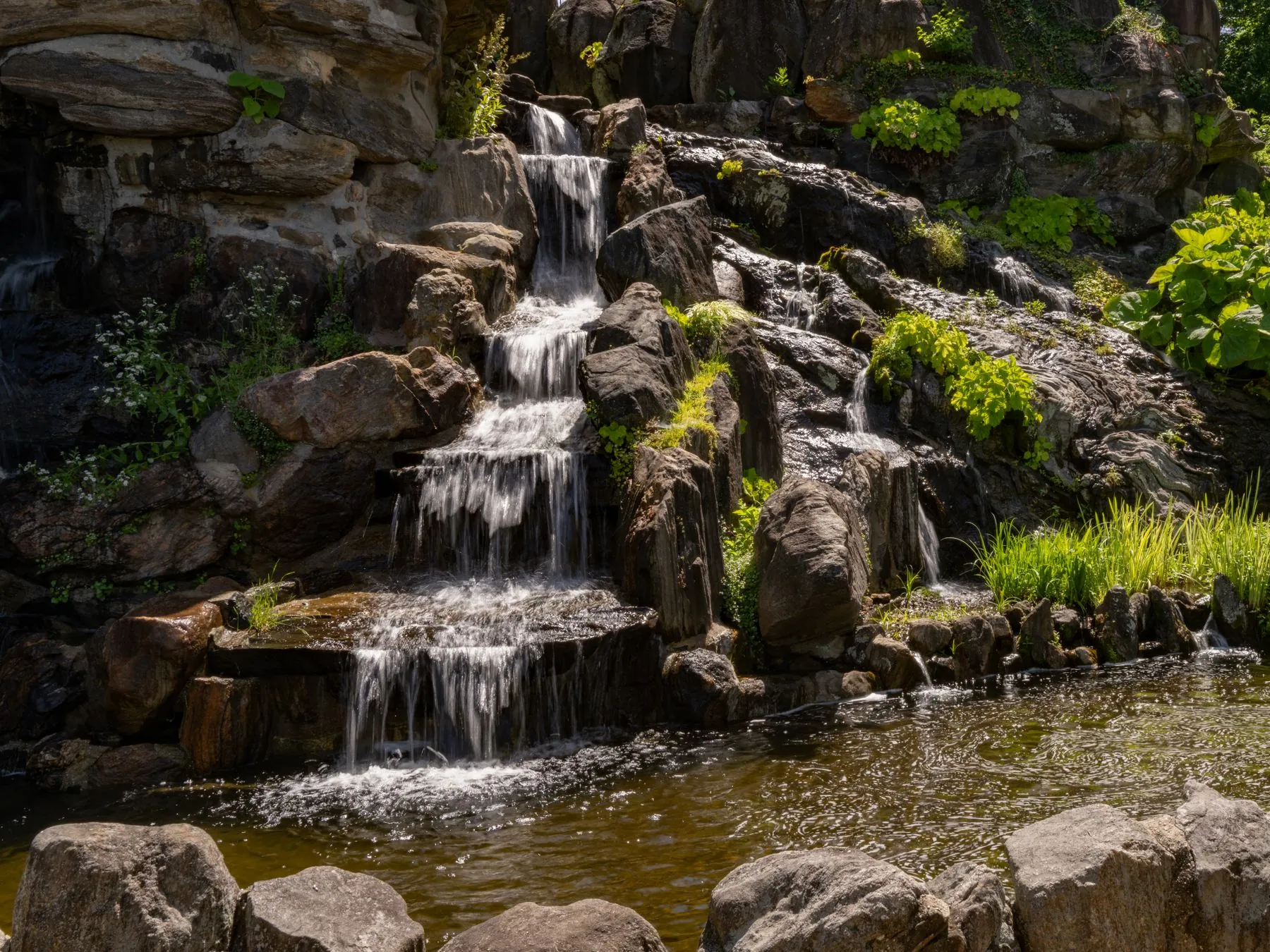 Natural rock waterfall cascading through a planted private garden in Al Ain, built by Absher Landscaping from locally quarried stone